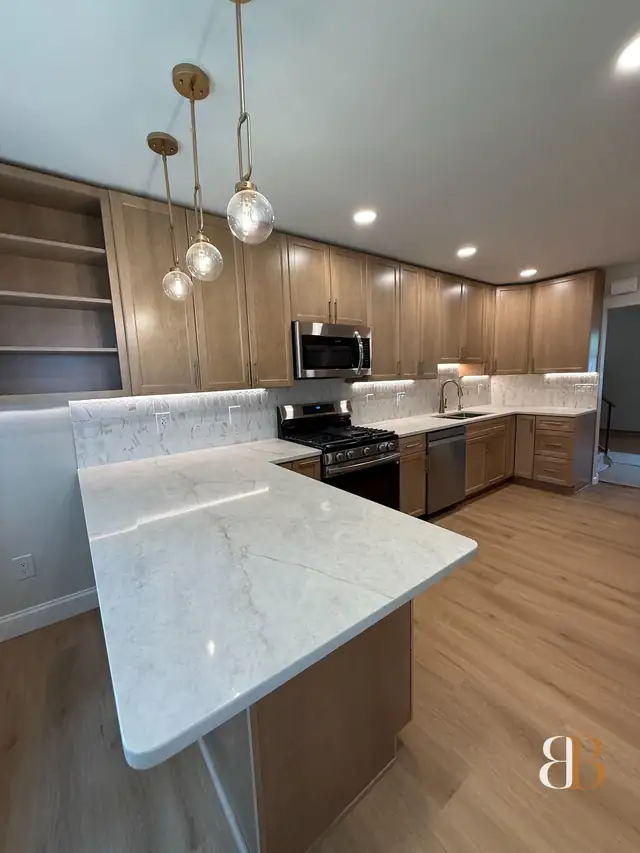 Bala Cynwyd kitchen with a white stone peninsula, natural maple cabinets, glass globe pendants, a gas range and light wide-plank floors