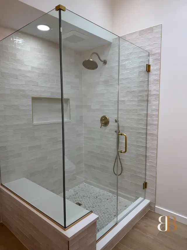 Fort Washington bathroom with a frameless glass shower, white stacked wall tile, a recessed niche, a built-in bench and brushed brass fixtures
