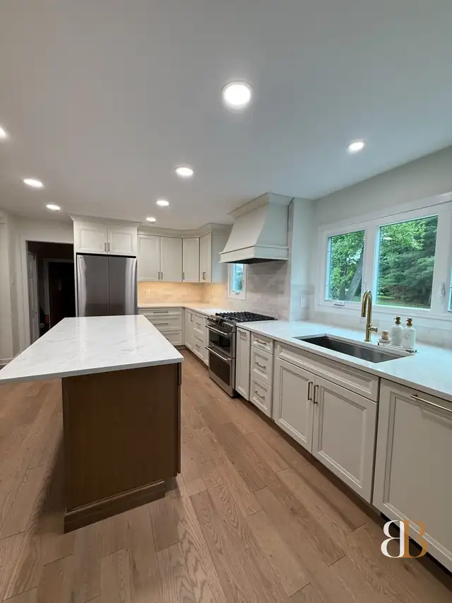 Fort Washington kitchen with white cabinets, a white stone island on a stained wood base, a white range hood, under-cabinet lights and a stainless refrigerator