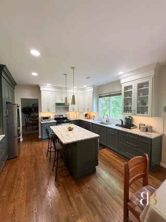 Doylestown kitchen with sage green lower cabinets and island, vanilla glass-front upper cabinets, brass pendants and a wide window over the sink