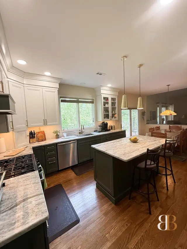 Open Doylestown kitchen with sage green cabinets and island, white glass-front uppers, brass pendants and windows over the sink