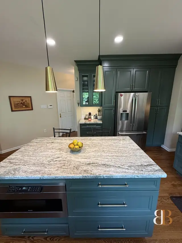 Painted sage island with a granite top and a built-in microwave drawer in a Doylestown kitchen, with brass pendants above